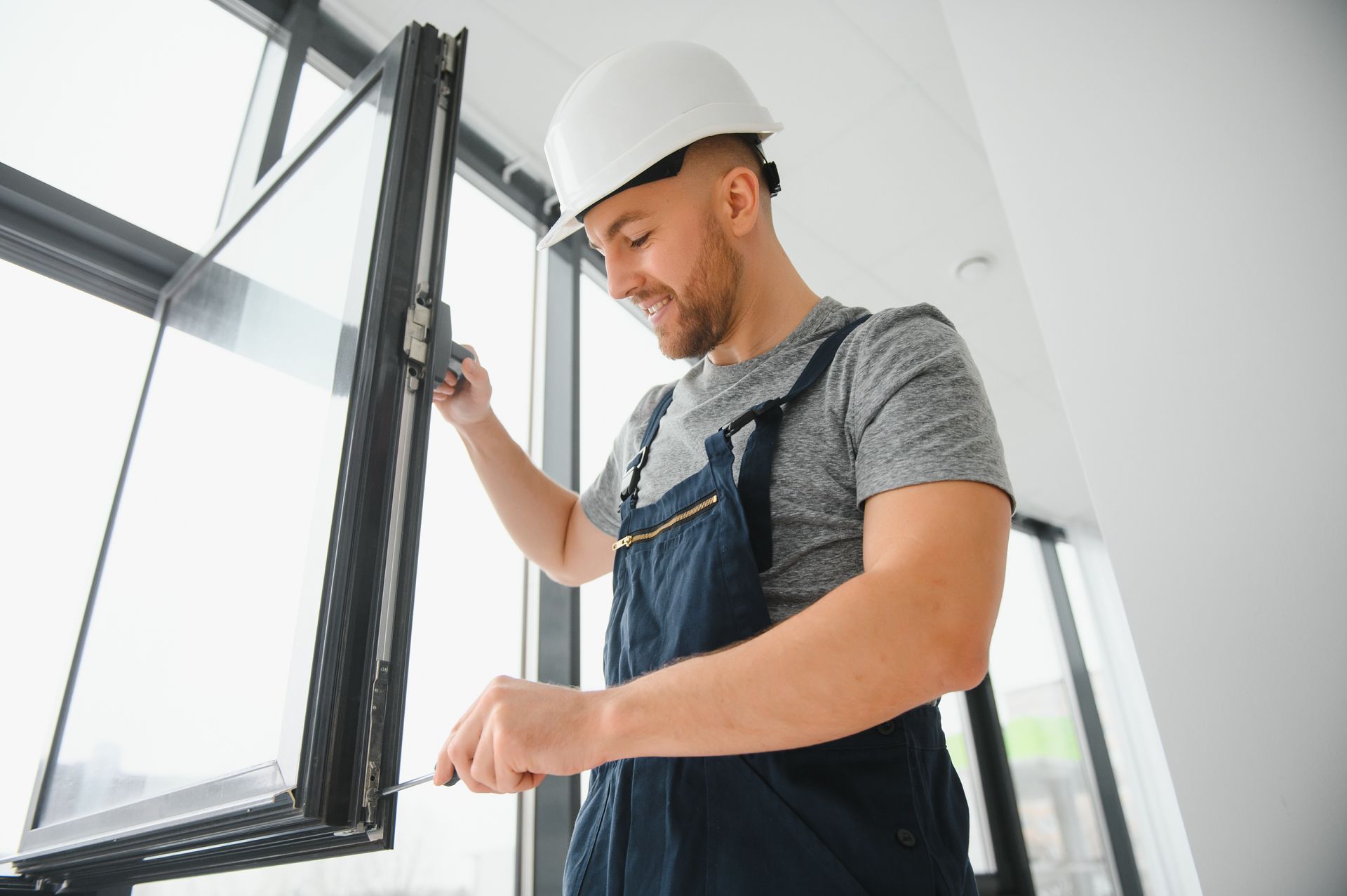 Worker in a hard hat measuring a window frame at a bright construction site