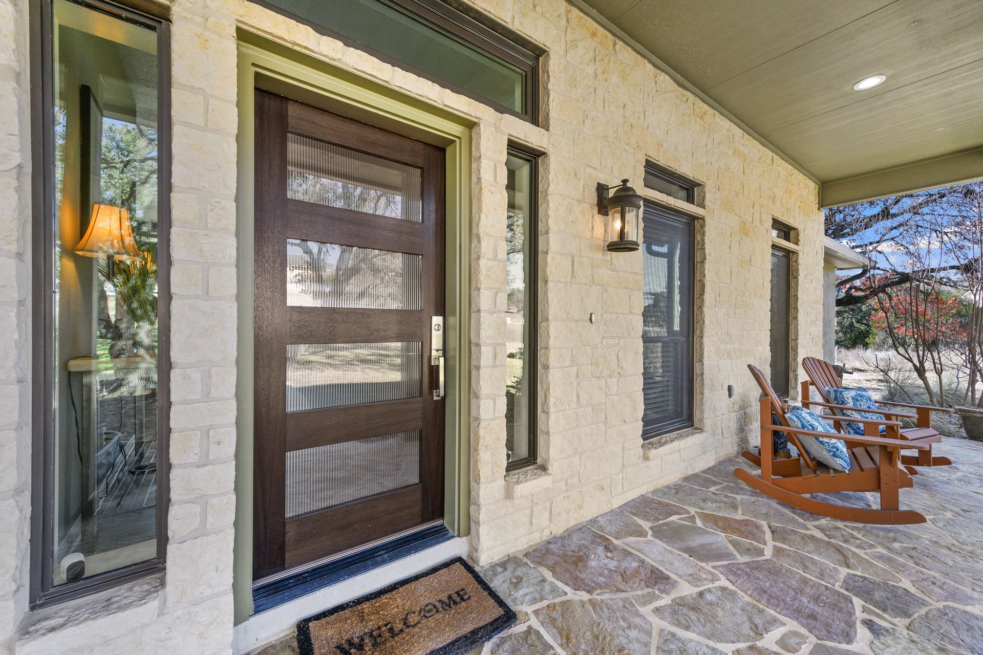 Front porch with dark wooden front door, stone walkway, and patio chairs beside the house Front porch with dark wooden front door, stone walkway, and patio chairs beside the house