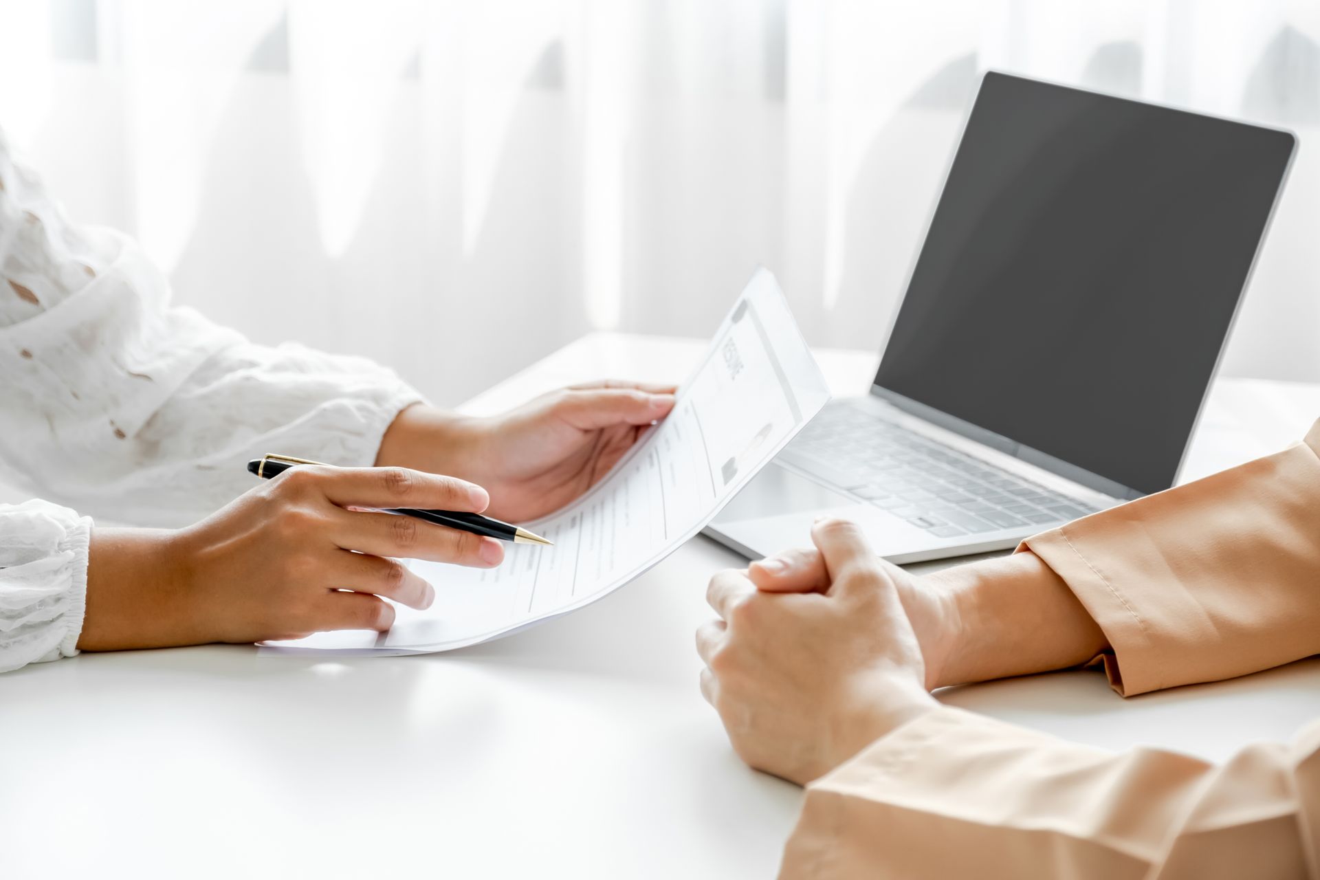 Two people reviewing documents and typing on a laptop at a bright table Two people reviewing documents and typing on a laptop at a bright table