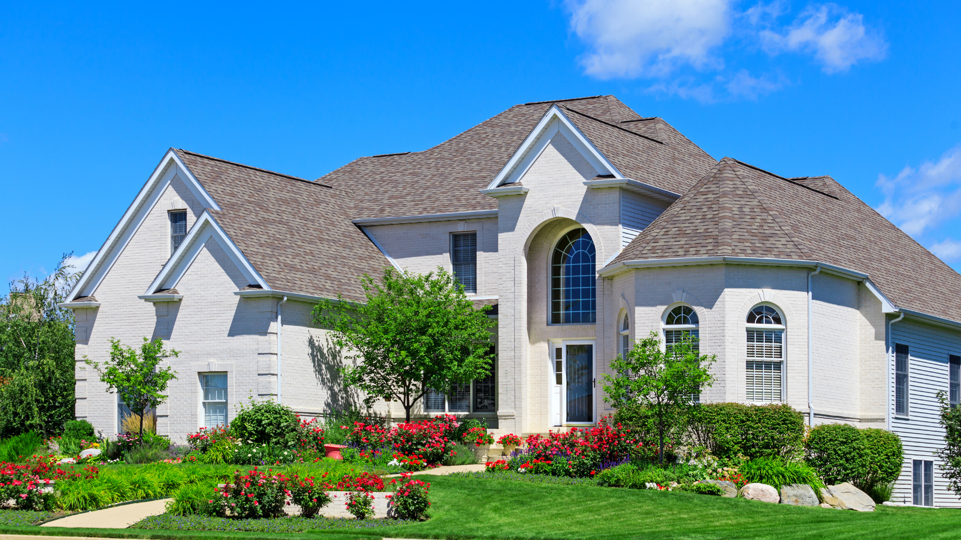 a large white house with a brown roof is sitting on top of a lush green lawn .
