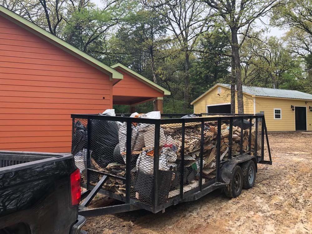 A trailer filled with logs is parked in front of a house.