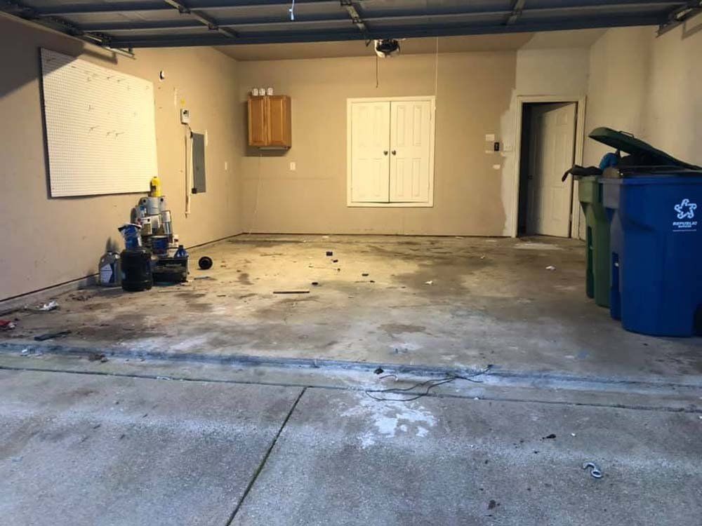 A dirty garage with a blue trash can in the middle of it.