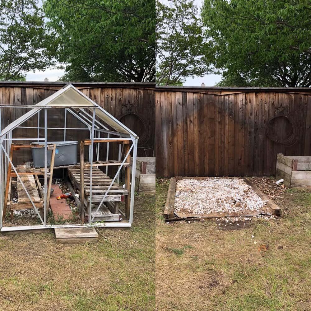 A greenhouse is sitting in the grass next to a wooden fence.