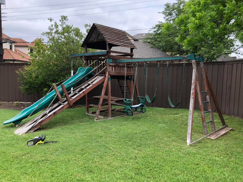 A wooden playground set with a slide and swings in a backyard.