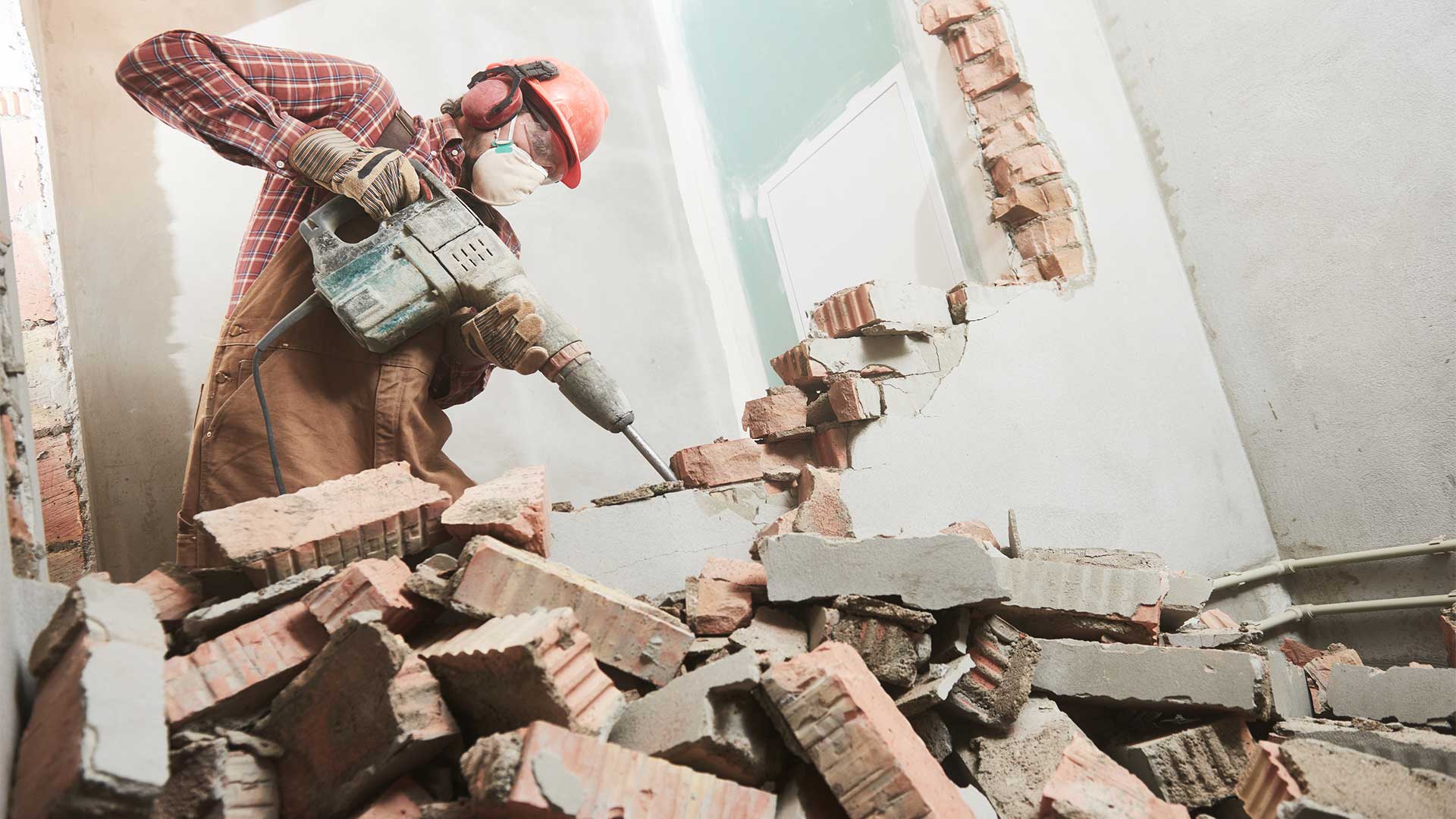 A man is breaking a brick wall with a hammer.