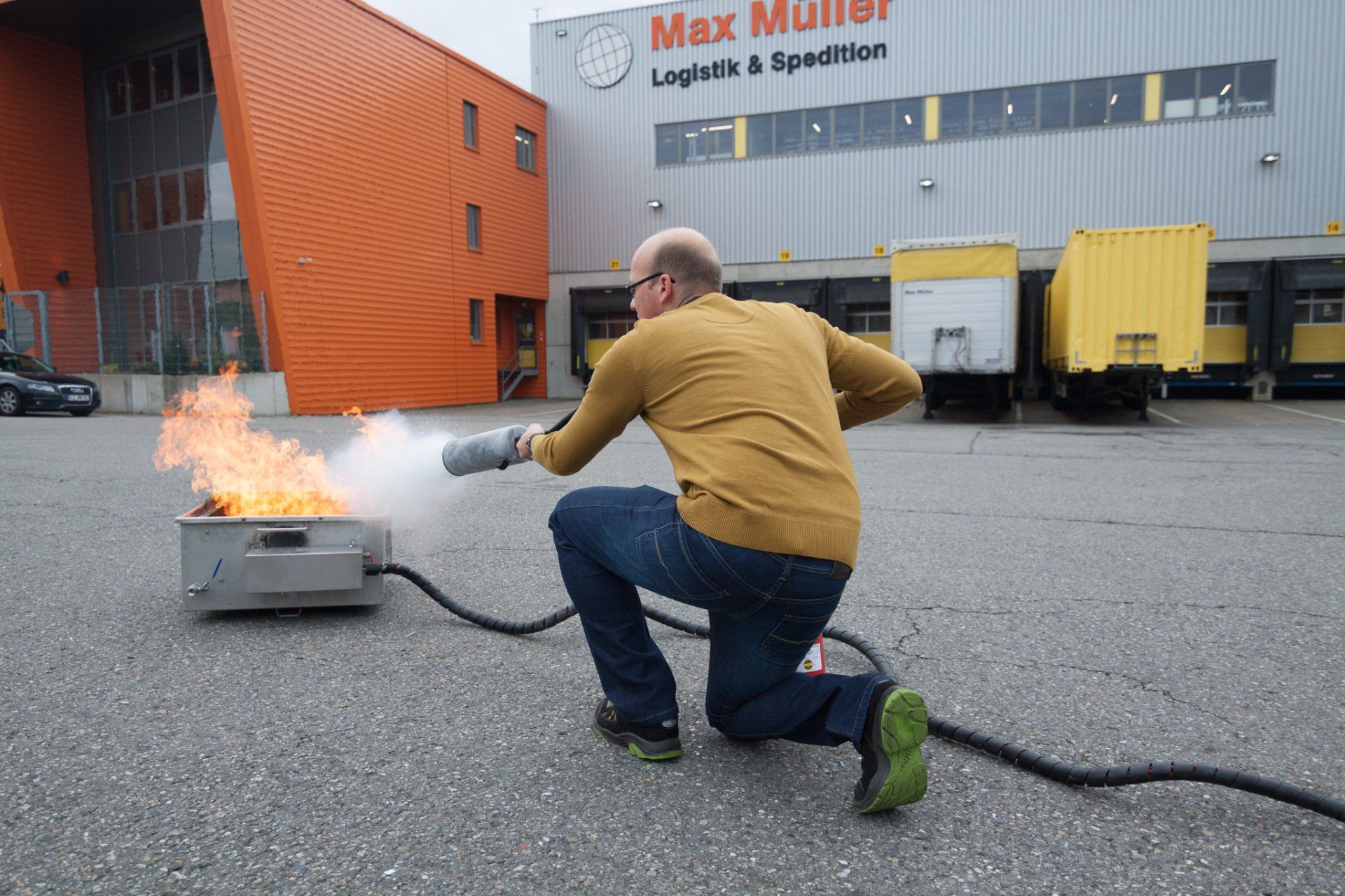 Ein Mann kniet mit einem Feuerlöscher vor einem Max-Müller-Gebäude.