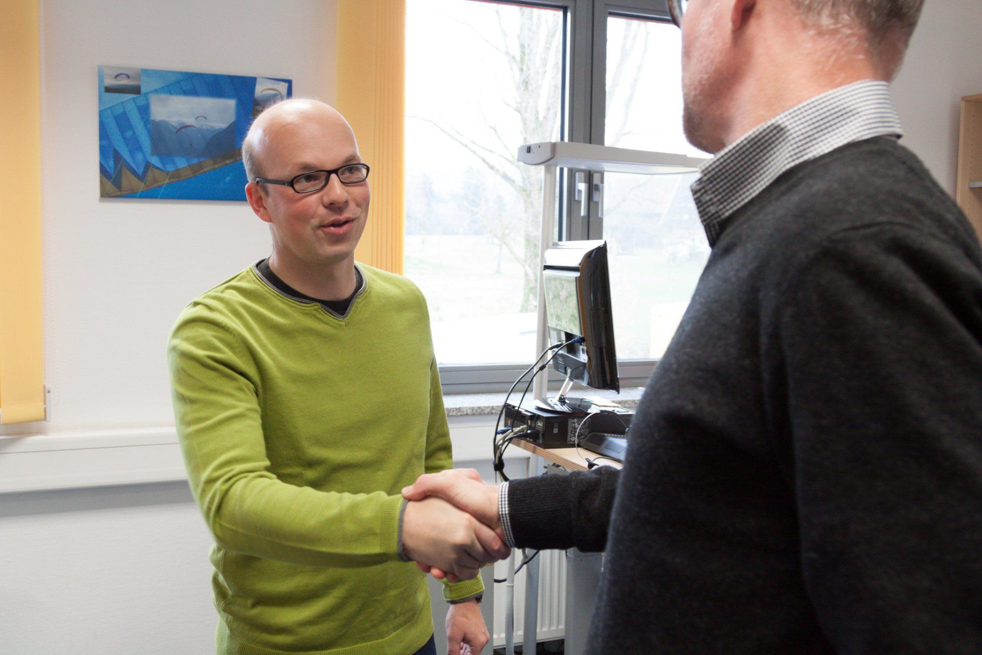 Ein Mann in einem grünen Pullover schüttelt einem anderen Mann die Hand