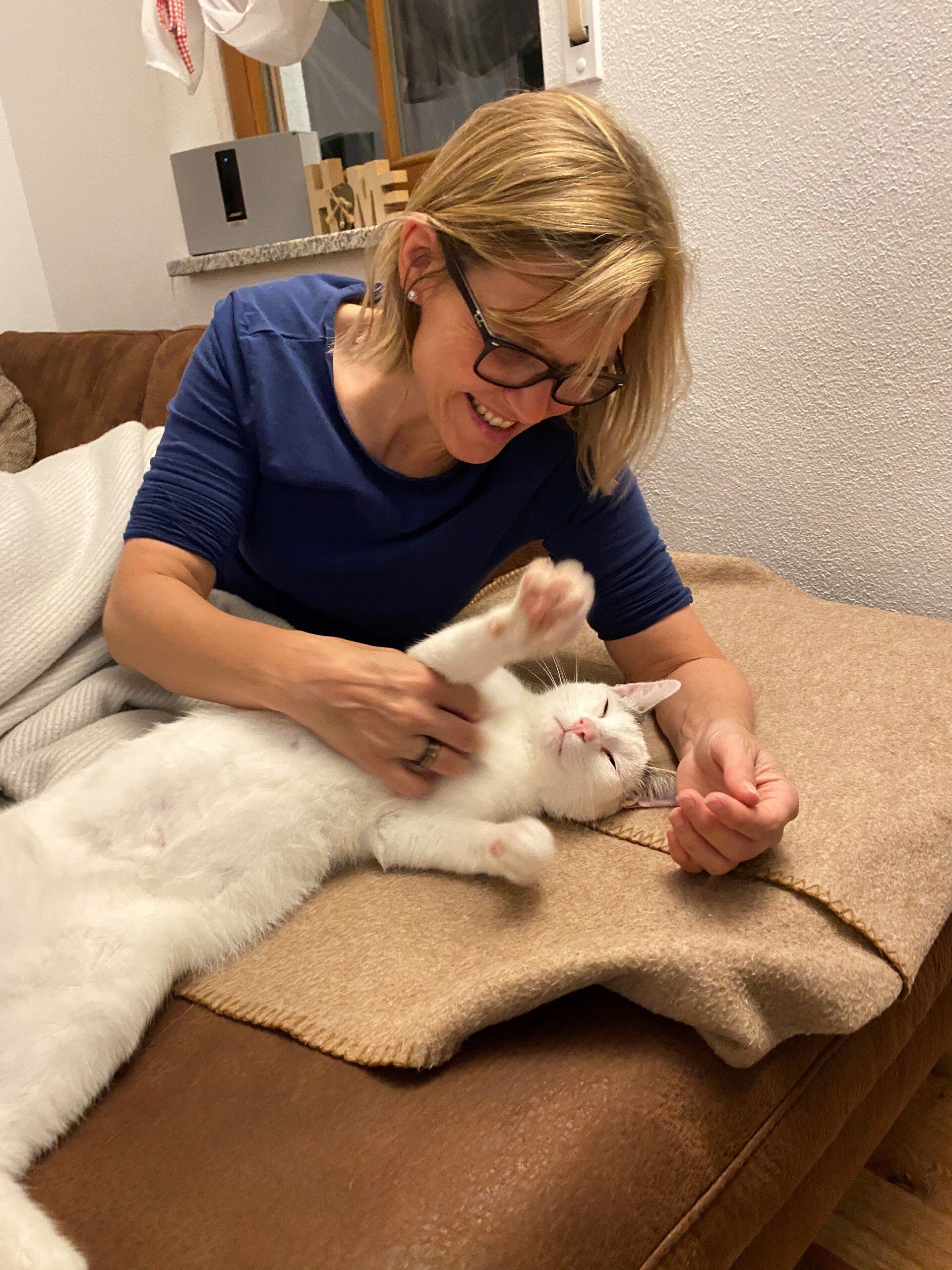 Eine Frau streichelt eine weiße Katze auf einem Sofa.