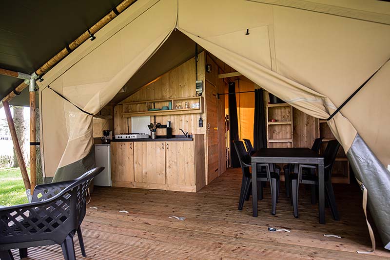 Interieur van een glampingtent van canvas met houten keuken, tafel, stoelen en een gevlochten bank.