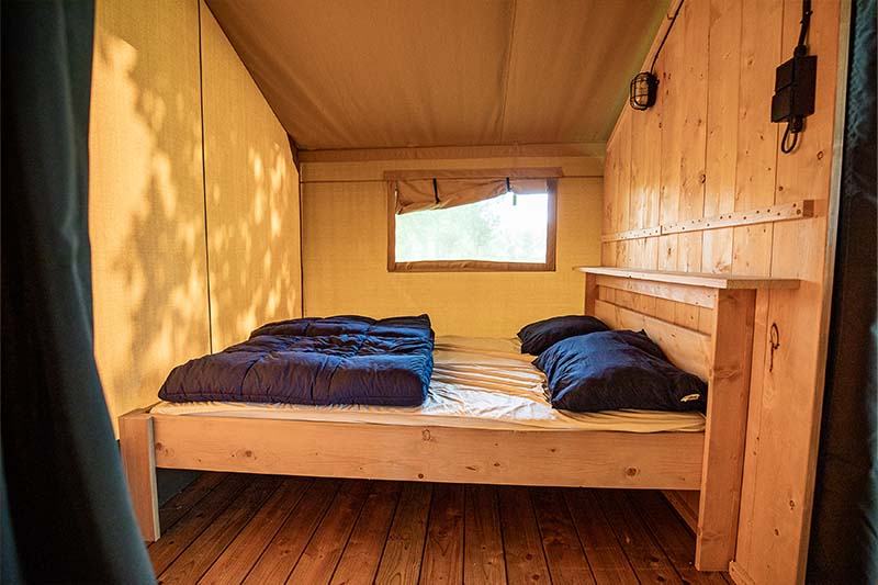 Gezellige slaapkamer in een houten blokhut met een bed, blauw beddengoed en een klein raam.