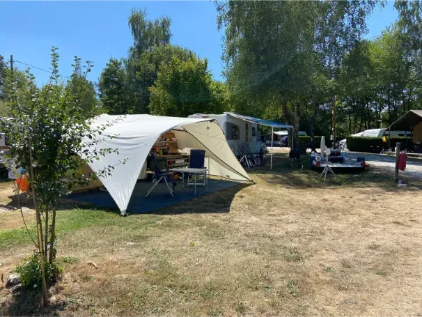 Kampeerterrein met witte partytent, picknicktafels, campers en mensen op een zonnig grasveld.