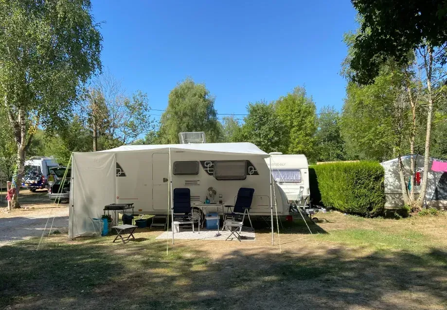 Kampeertent en luifel op een zonnige camping, met stoelen, tafel en bomen op de achtergrond.