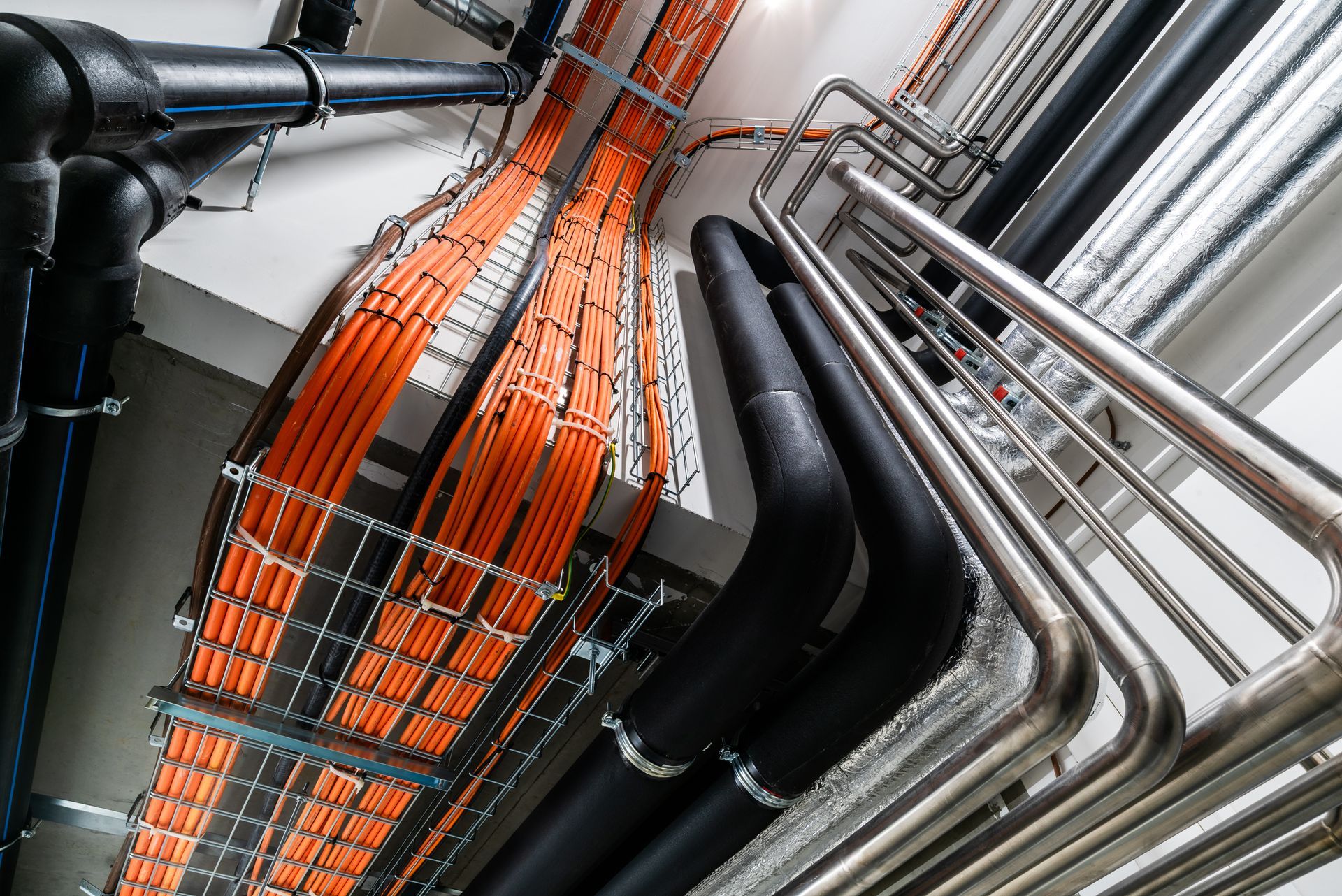 Orange and black cable tray with metal pipes and conduits in an industrial ceiling space. Orange and black cable tray with metal pipes and conduits in an industrial ceiling space.