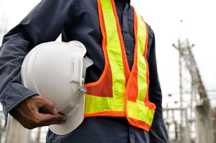 Construction worker holding a white hard hat, wearing a neon safety vest on a job site. Construction worker holding a white hard hat, wearing a neon safety vest on a job site.