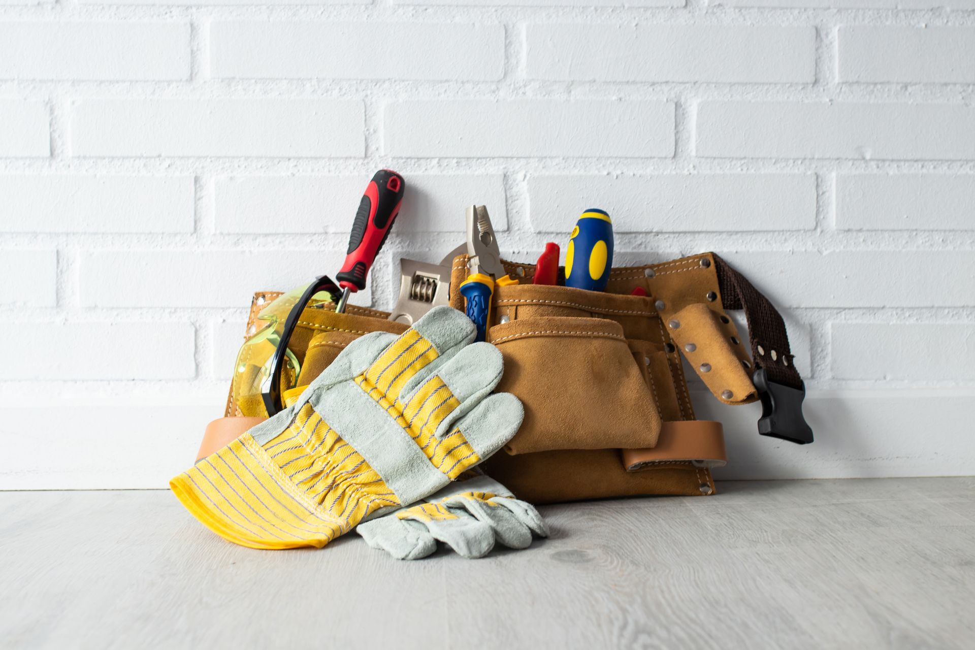 Tool belts with gloves and hand tools on a table against a white brick wall.