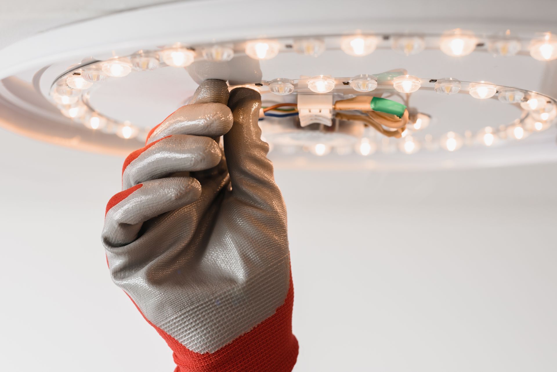 Gloved hand adjusting a ceiling light fixture with a screwdriver.