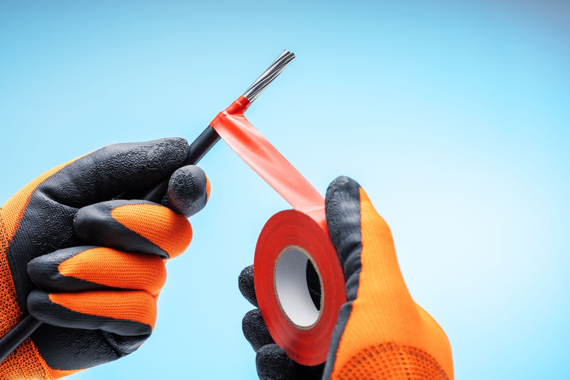 Hands in orange work gloves holding a utility knife and red tape on a blue background.