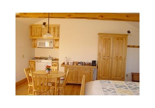 Rustic kitchen-dining room with wooden table, cabinets, and a bed in the foreground