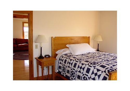 Bedroom with wooden bed, patterned quilt, bedside tables, and lamps, viewed through an open doorway