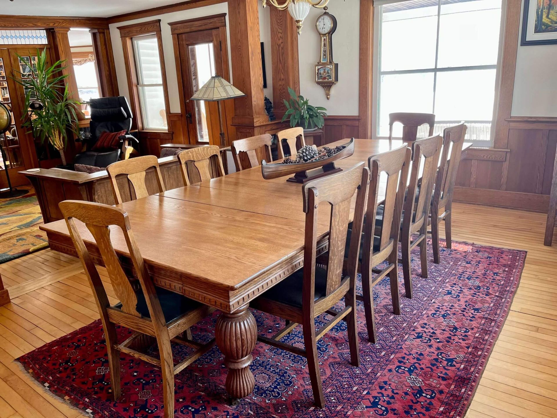 Dining room with large wooden table, chairs, area rug, and wood paneling.