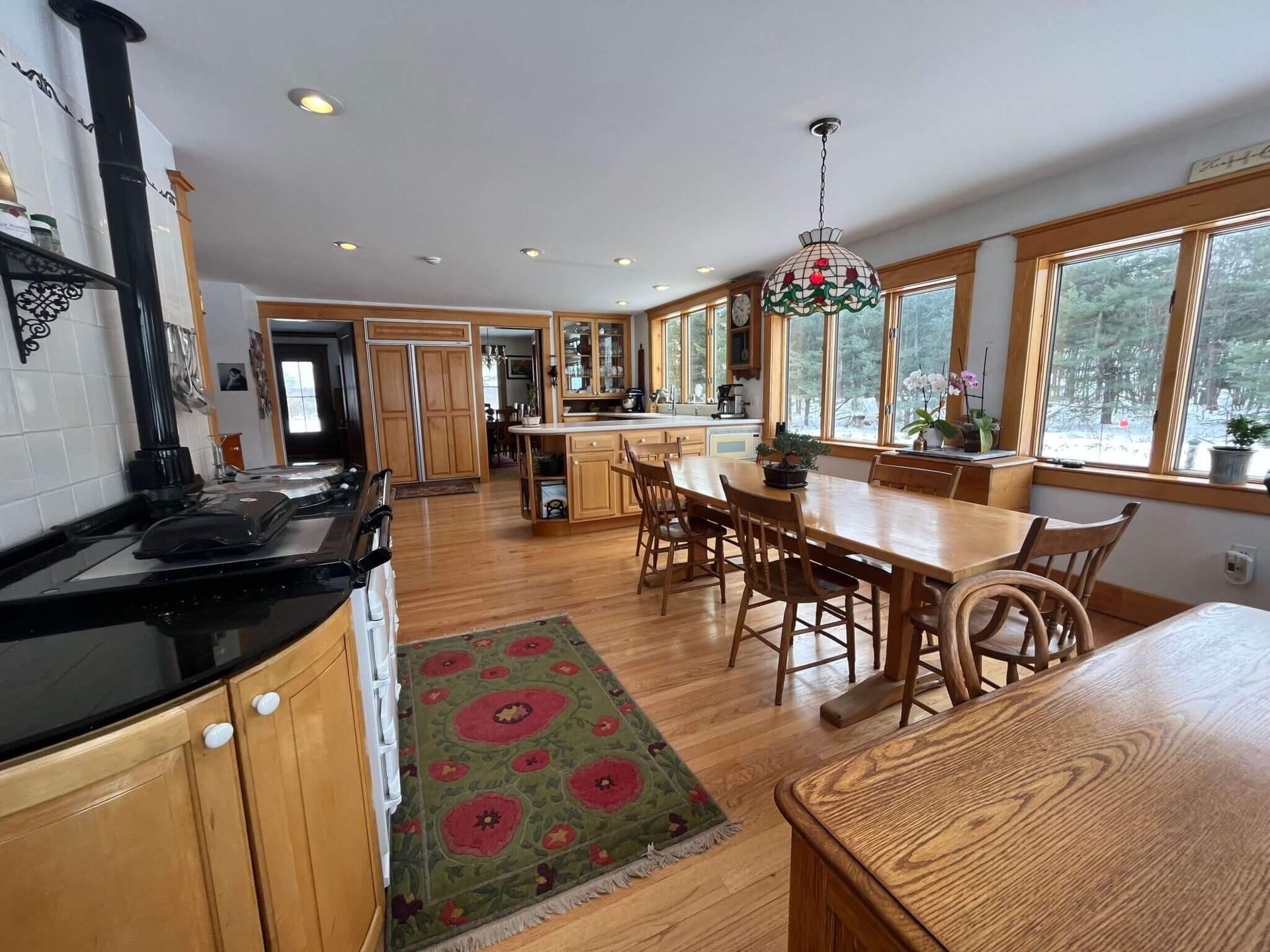 Spacious kitchen with a dining area; wood cabinets, stove, and table; large windows, wood floors and area rug.