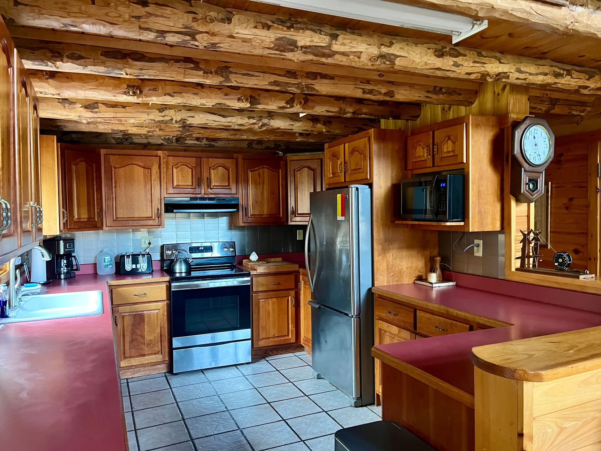 Rustic kitchen with wood cabinets, stainless fridge, stove, tiled floor, and red dining nook
