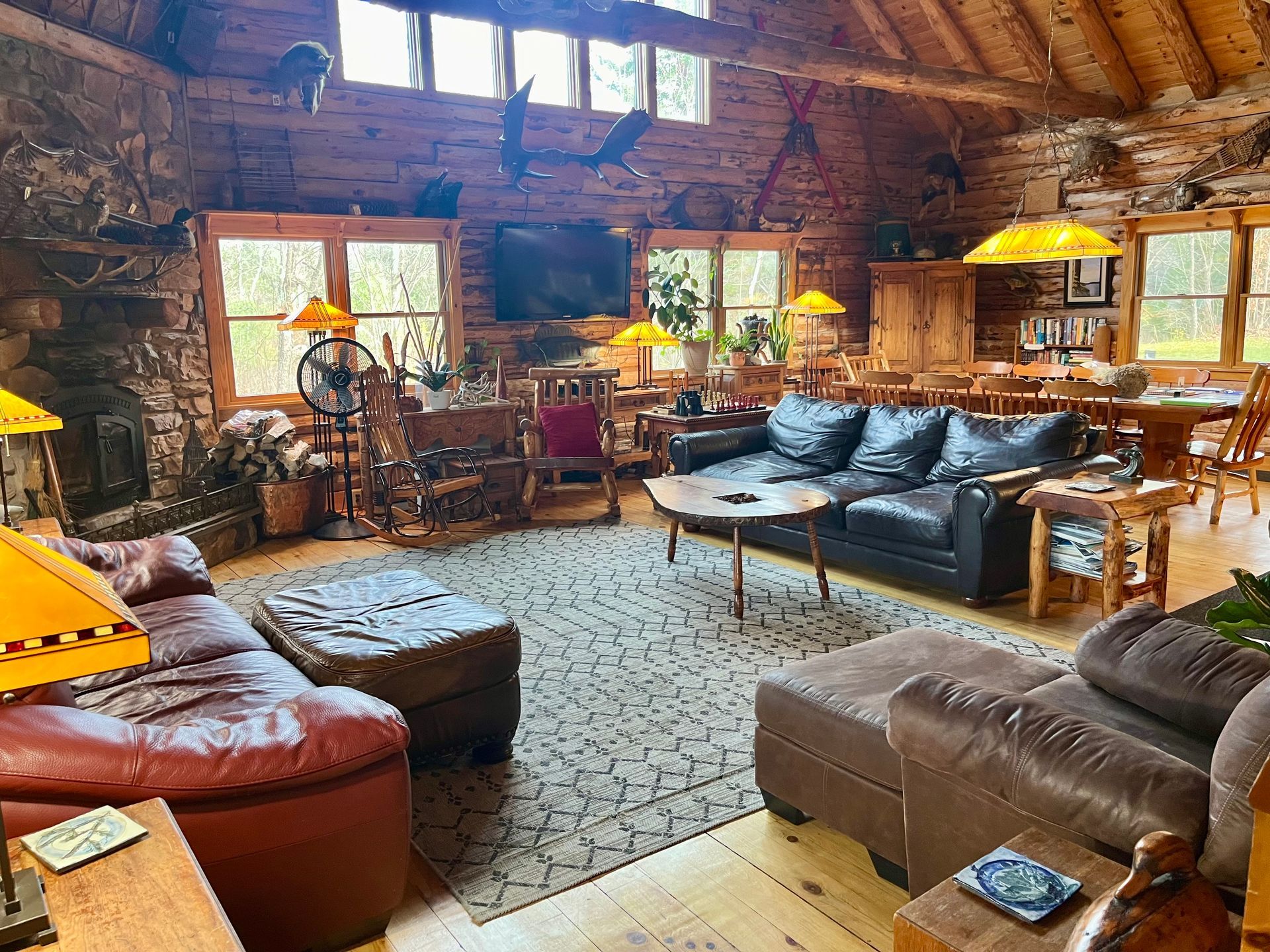 Cozy log cabin living room with leather sofas, wood beams, large windows, and rustic decor