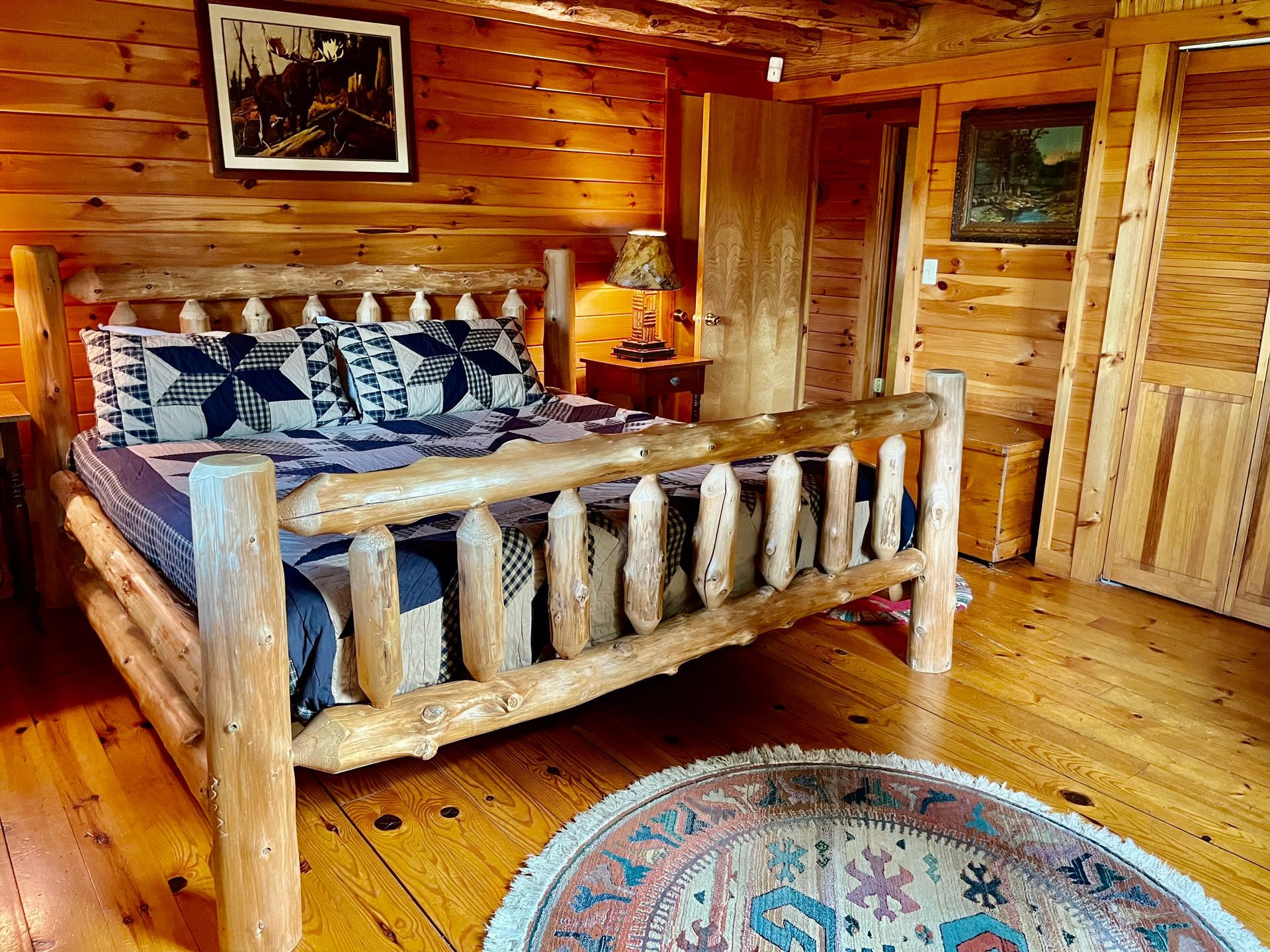 Rustic log cabin bedroom with wooden bed, plaid bedding, and round rug
