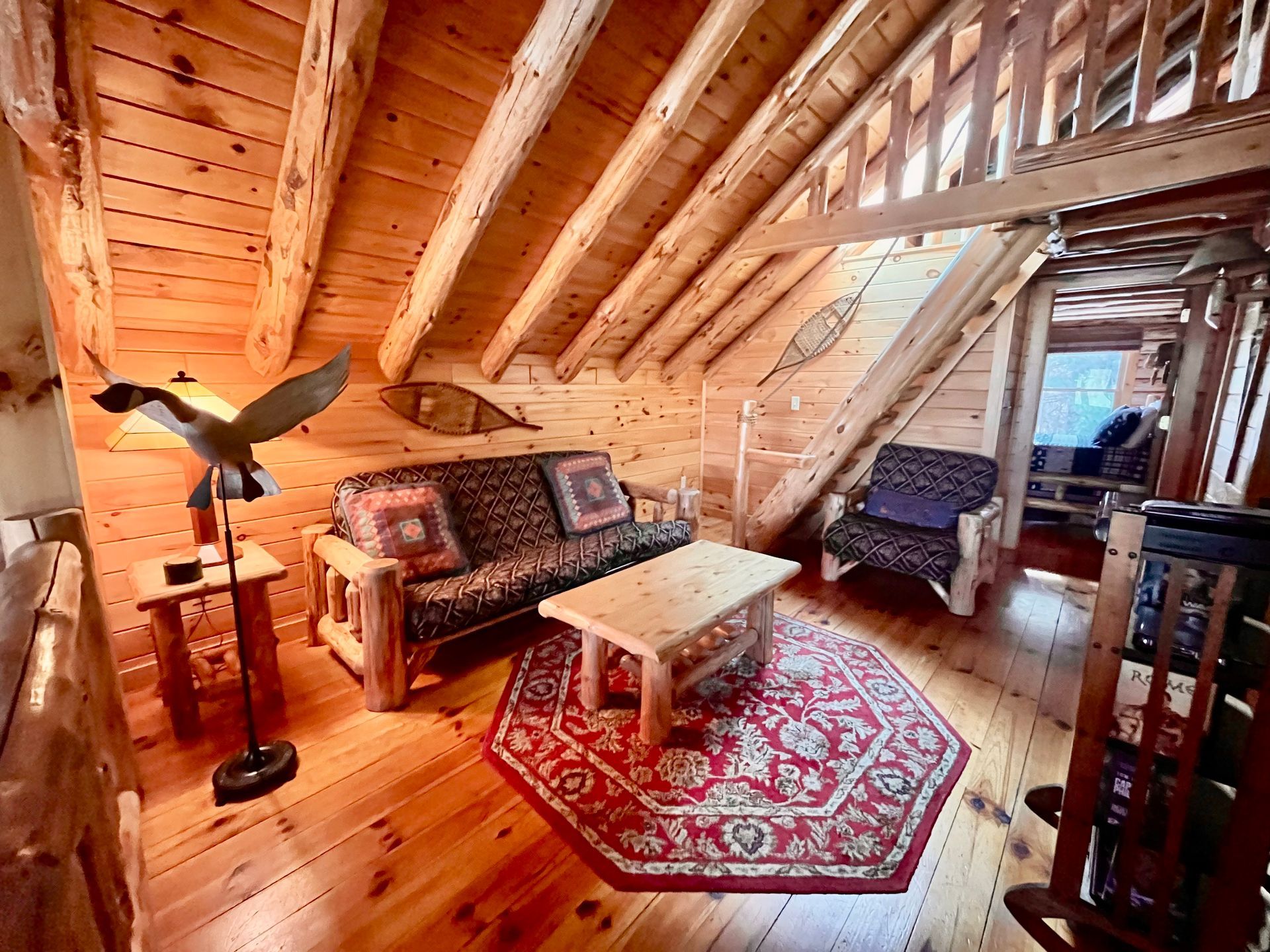Cozy attic living room with wooden walls, patterned rug, sofa, chair, coffee table, and bird sculpture lamp.
