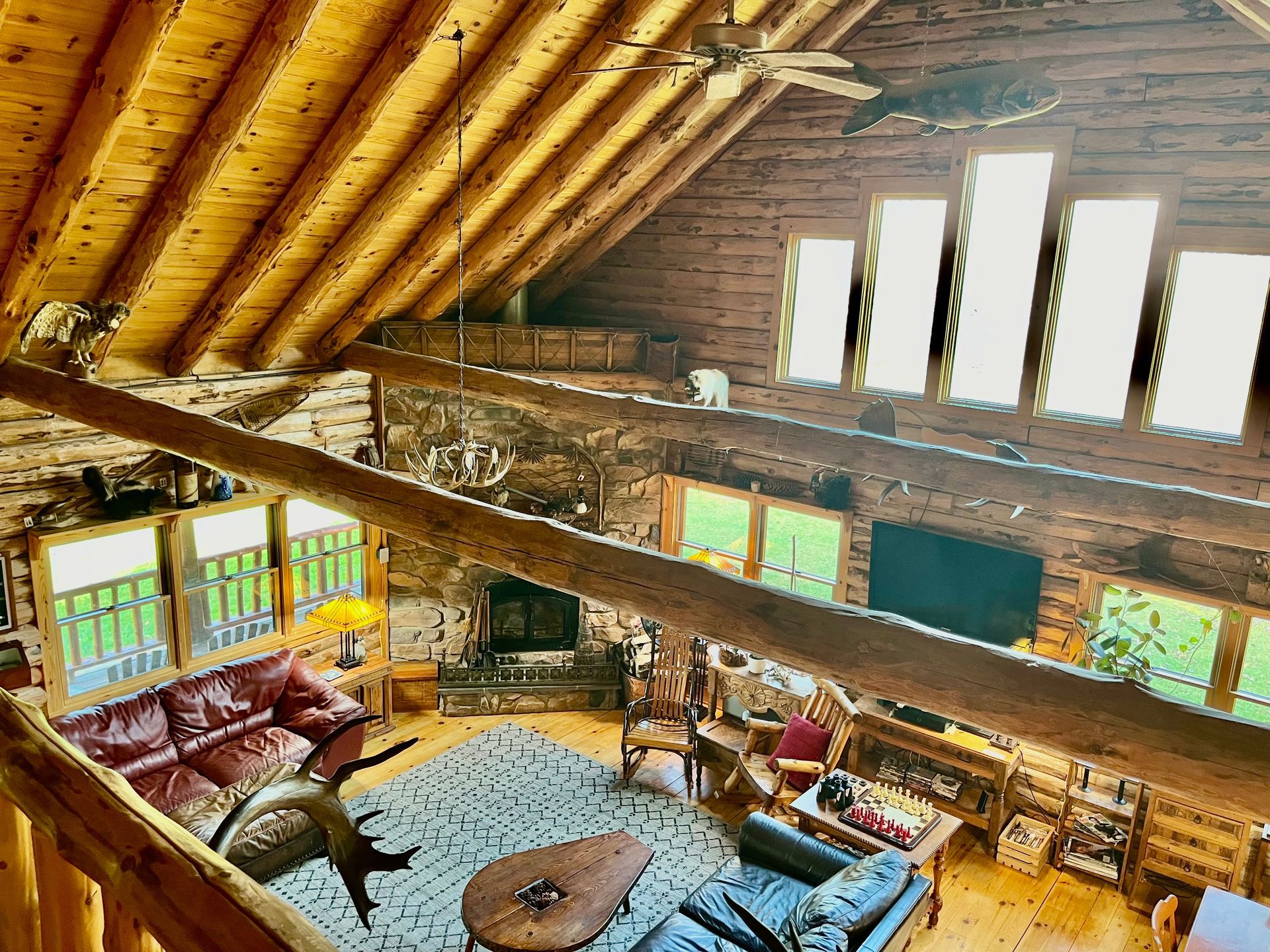 Rustic log cabin living room with curved wooden ceiling, large windows, stone fireplace, and sofas around a rug