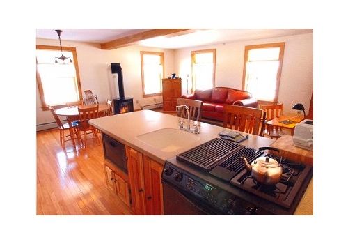 Modern kitchen with wood cabinets, island countertop, and dining area with red chairs by sunlit windows