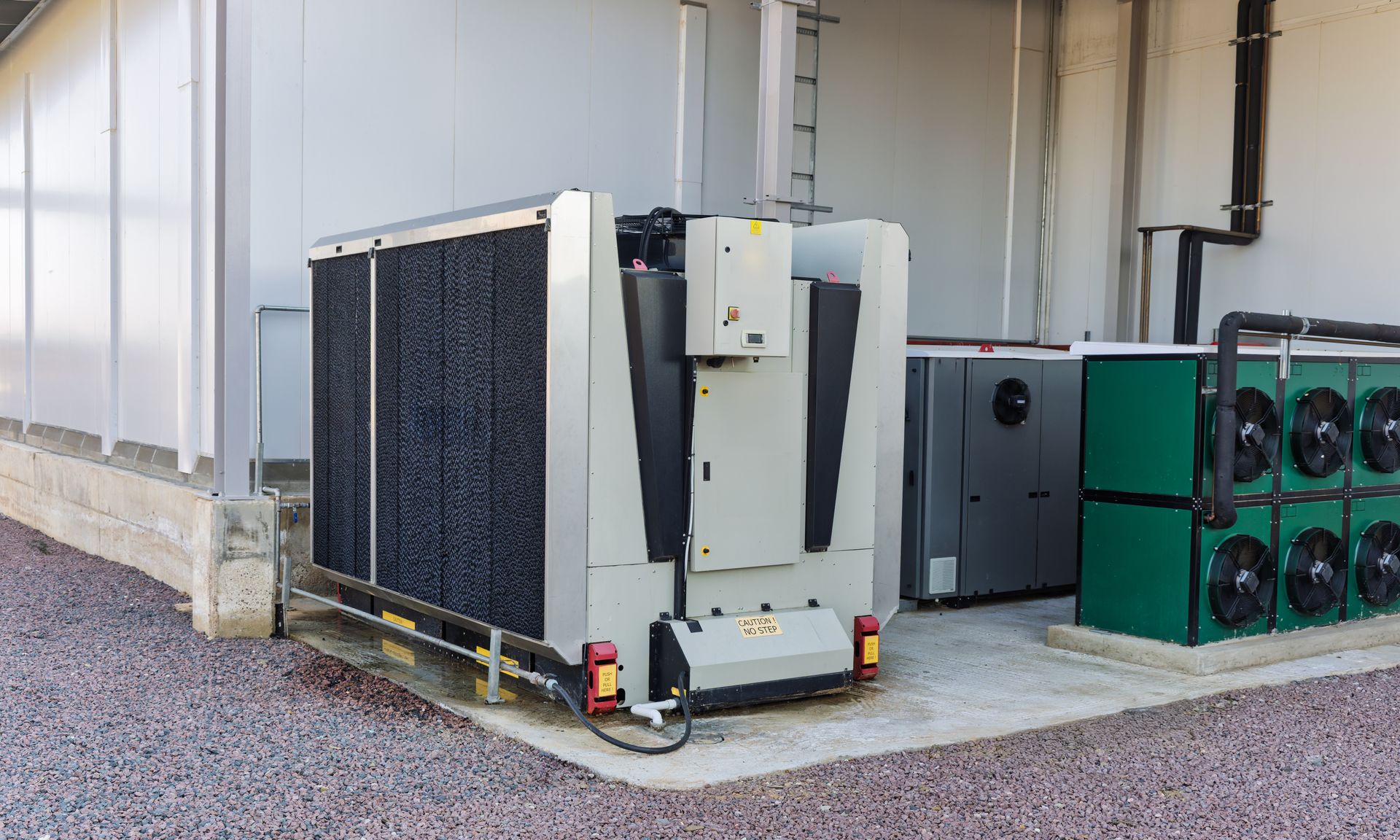Industrial air conditioning units outside a building on gravel.