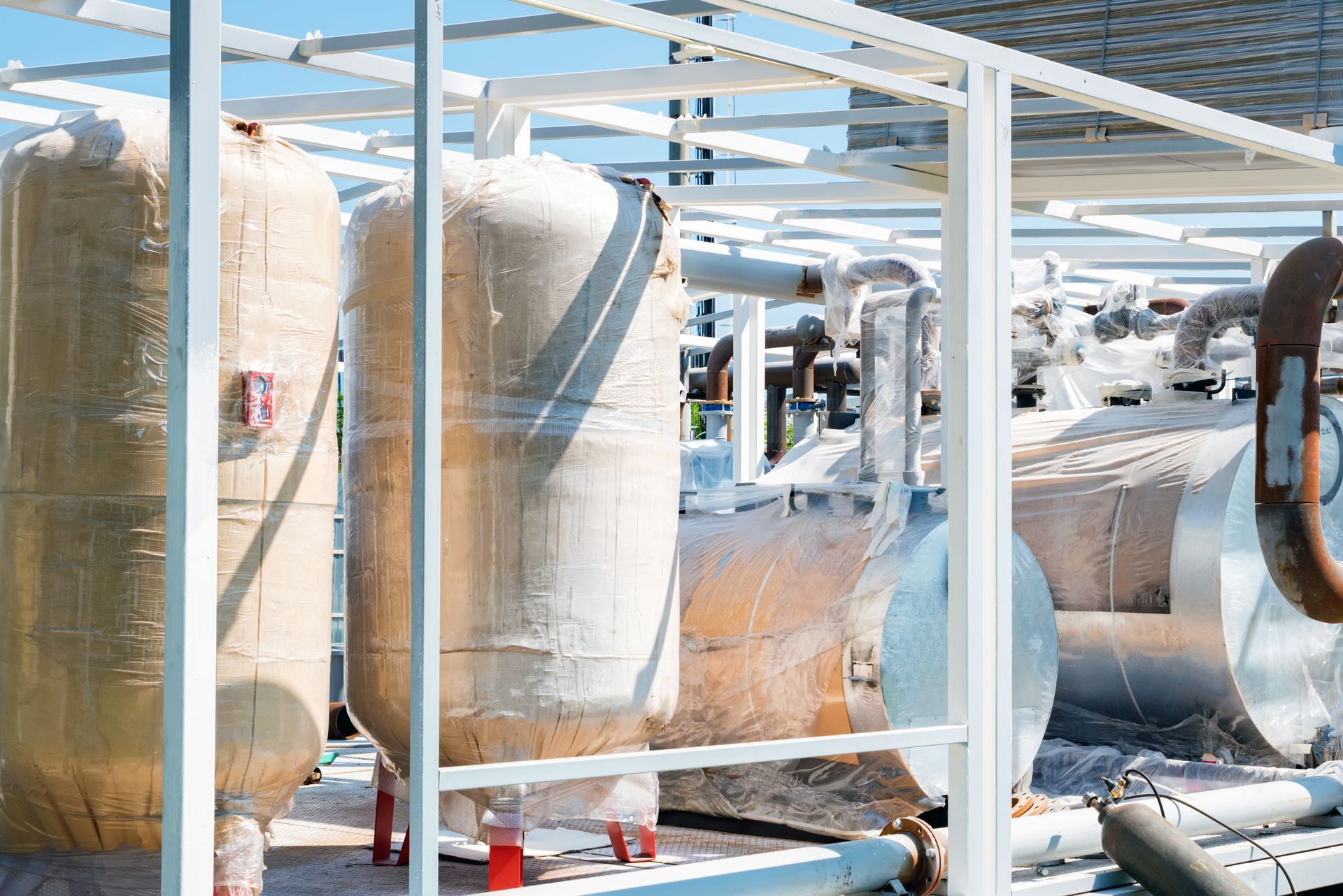 Industrial tanks and pipes, likely part of a processing plant, outdoors under a blue sky.