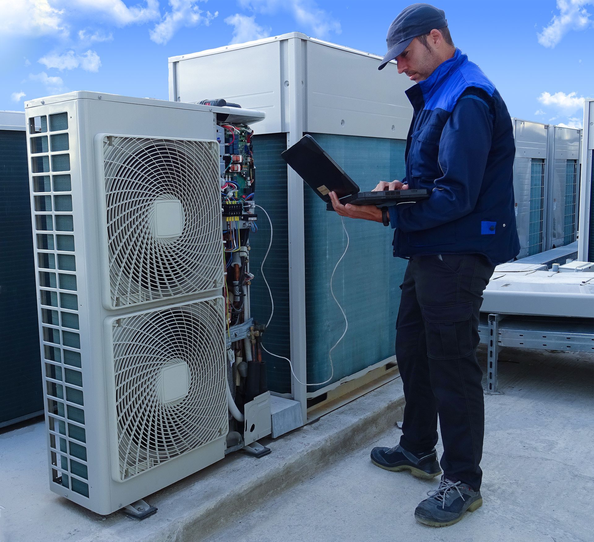 HVAC technician on a rooftop, using a laptop to inspect an air conditioning unit.