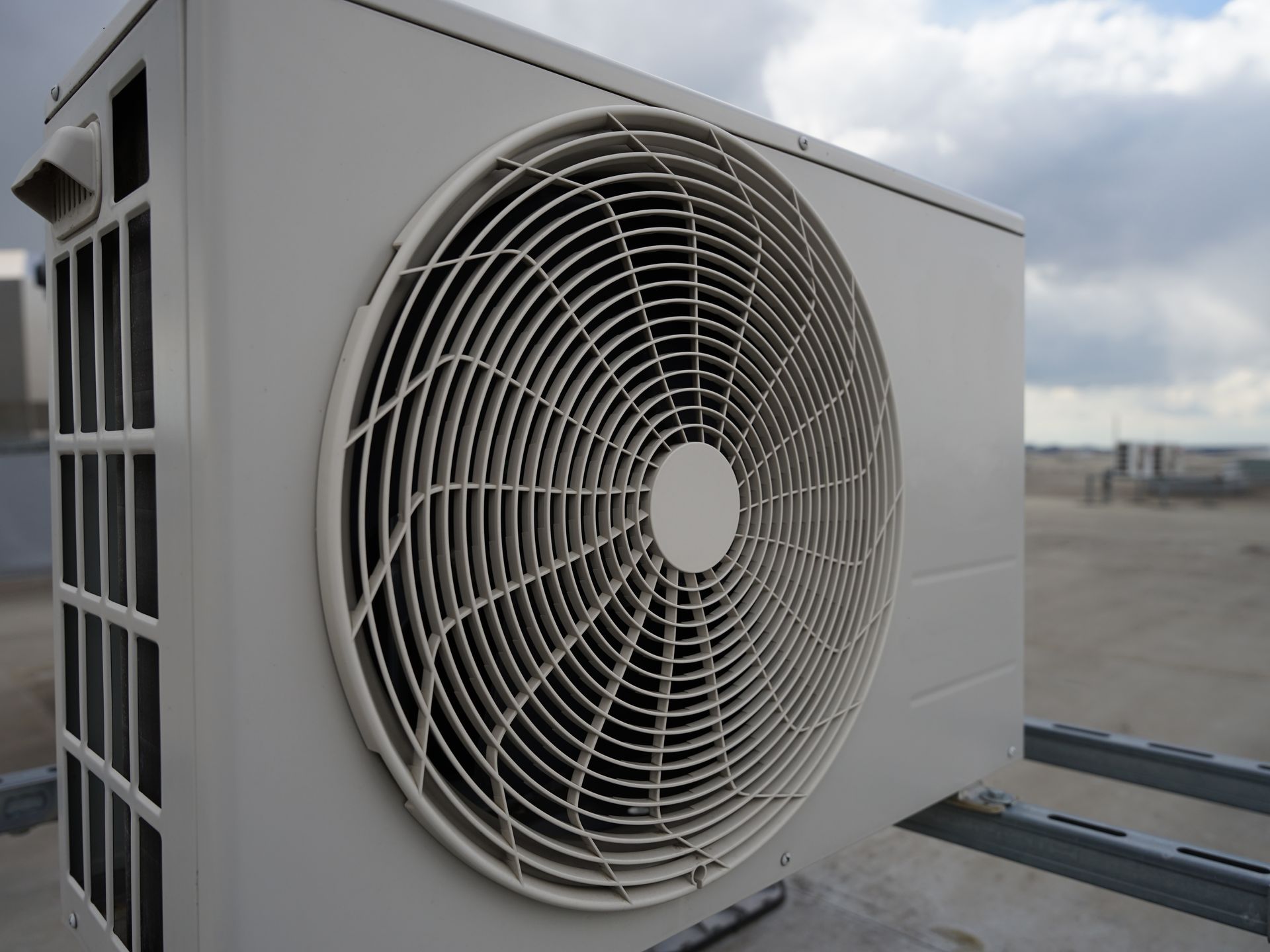 Beige outdoor air conditioning unit mounted on a metal frame against a cloudy sky. Beige outdoor air conditioning unit mounted on a metal frame against a cloudy sky.