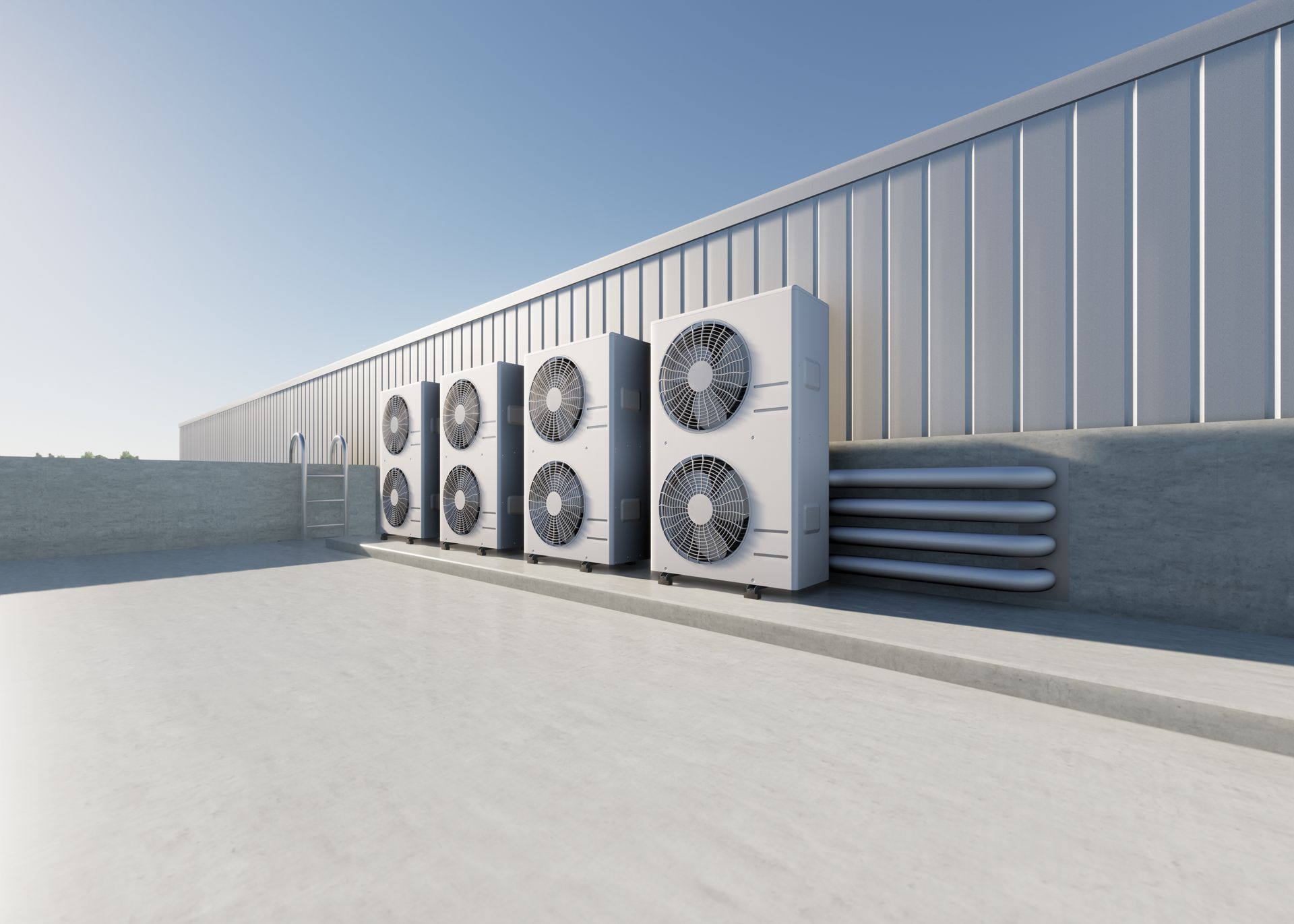 Four outdoor air conditioning units stand in a row on a flat gray roof against a large metal industrial building.