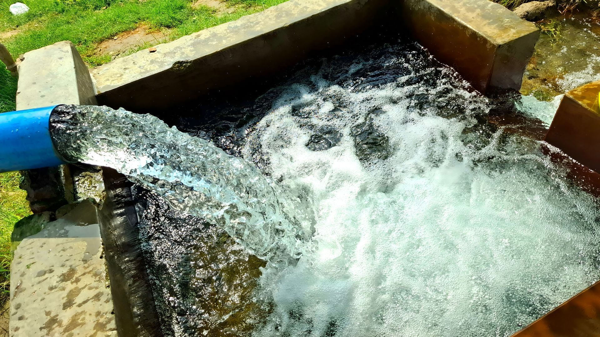 Water gushing from a blue pipe into a concrete basin, creating splashing foam outdoors Water gushing from a blue pipe into a concrete basin, creating splashing foam outdoors
