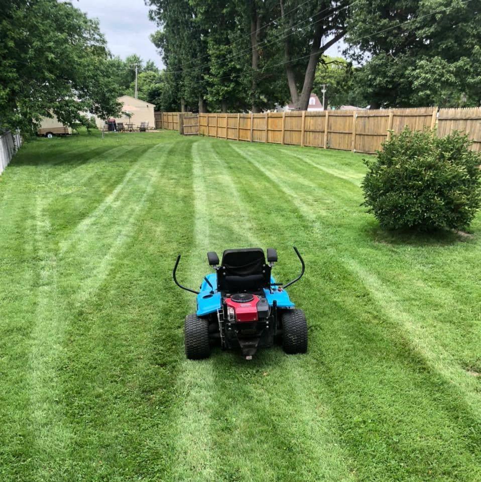 Red riding mower on a striped green lawn in a fenced backyard