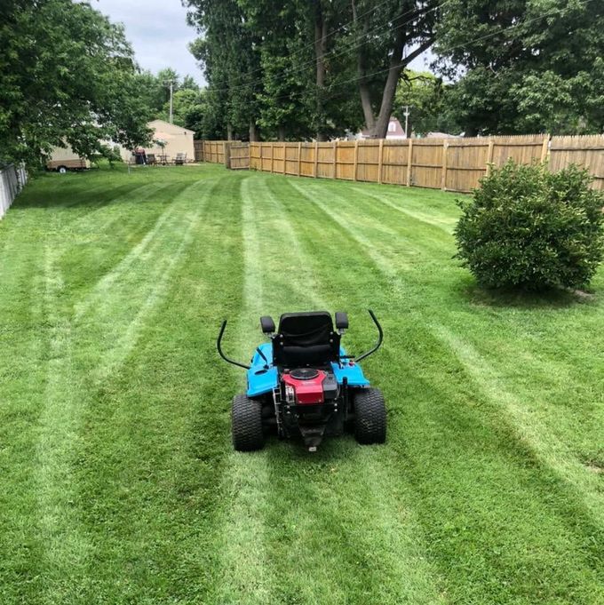 Red lawn mower on a striped green backyard lawn with a wooden fence and trees in the background