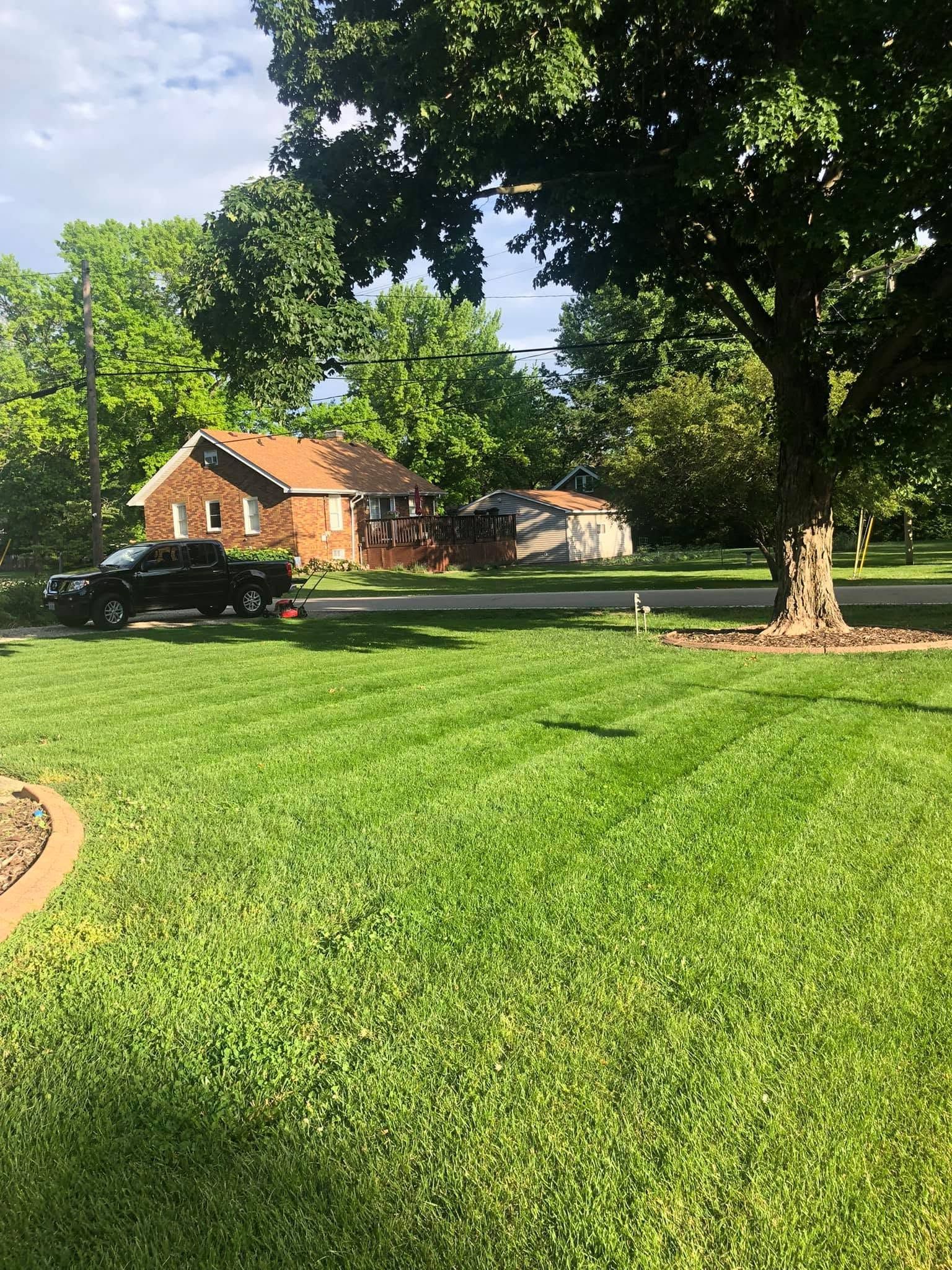 Brick house with a black car, large green lawn, and tall trees on a sunny day