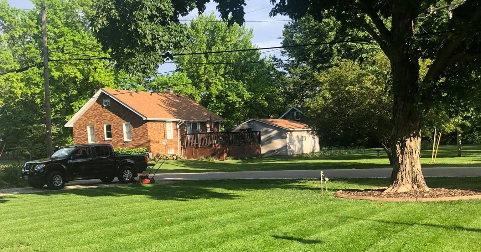 Brick house with a car parked in front, surrounded by green lawn and trees on a sunny day