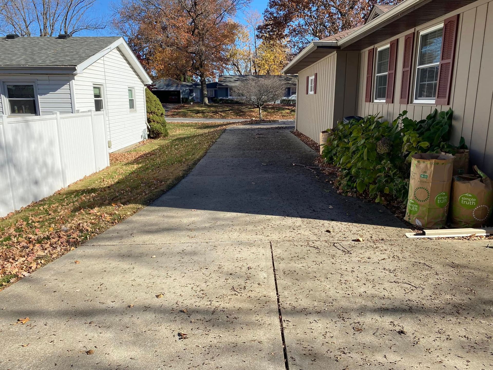 Driveway between two houses with autumn trees and potted plants by the right-side wall.