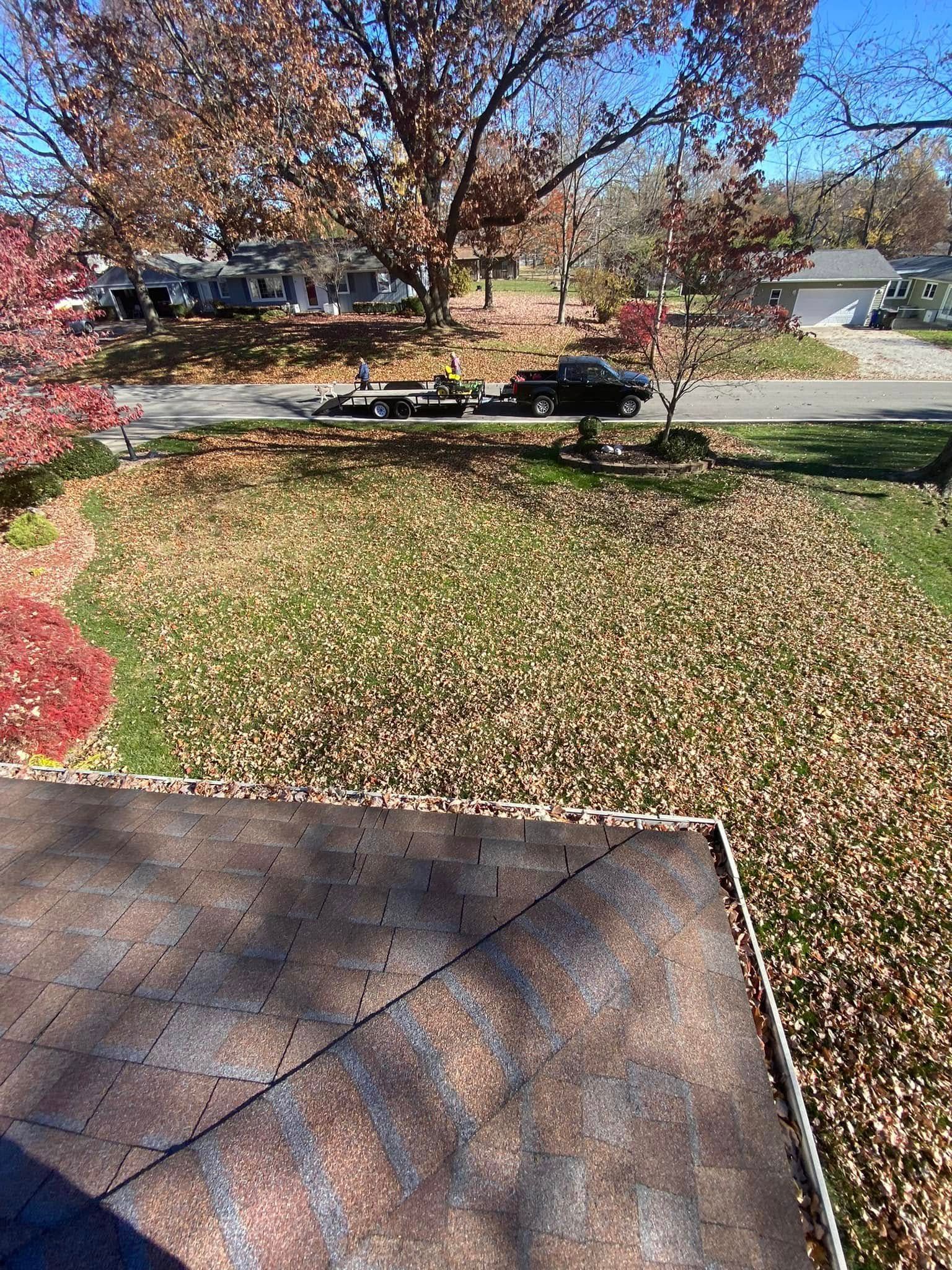 Autumn front yard with fallen leaves, a tree, and a porch edge in the foreground.