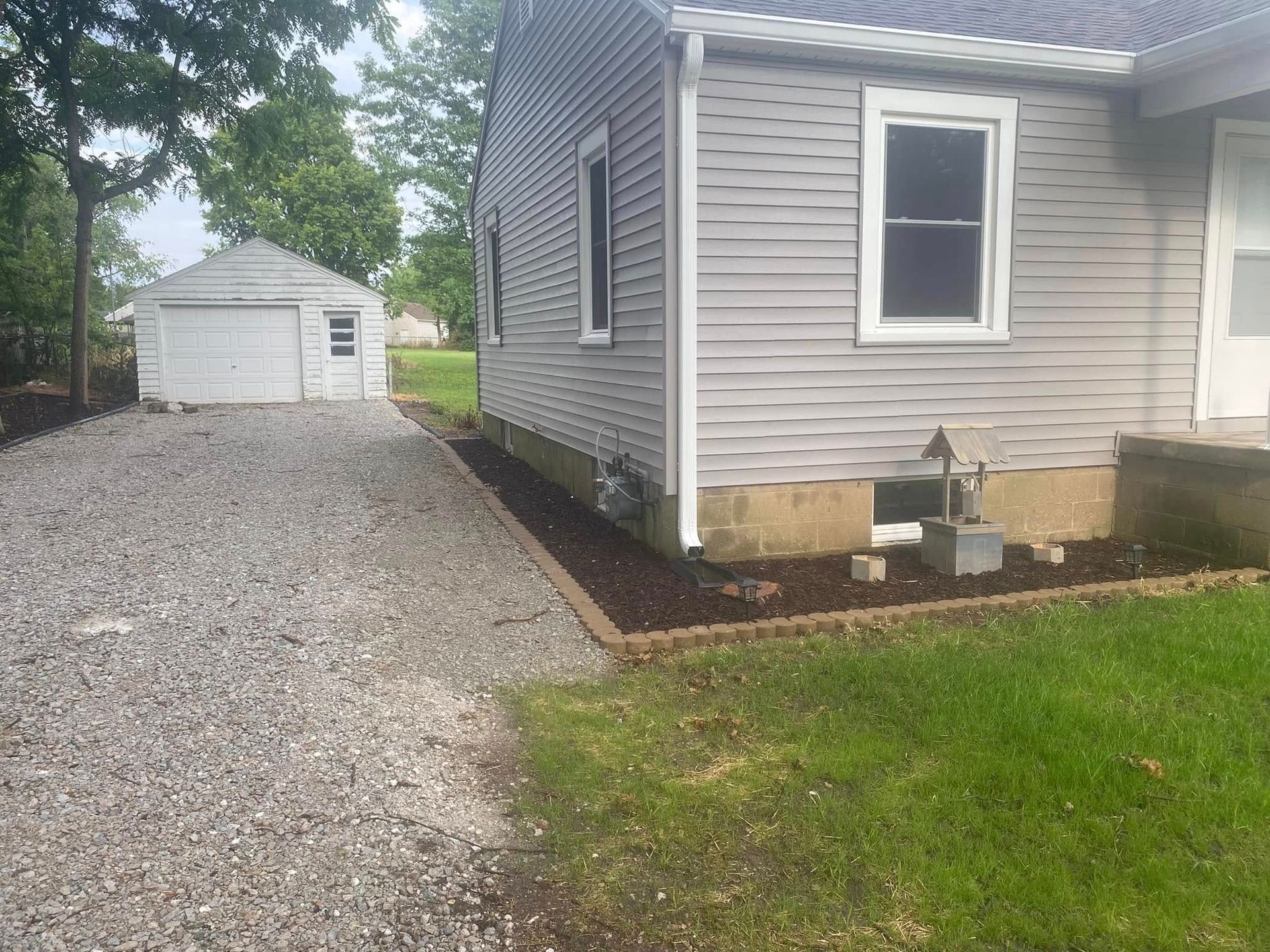Gravel driveway beside a gray house, with a white detached garage in the background.