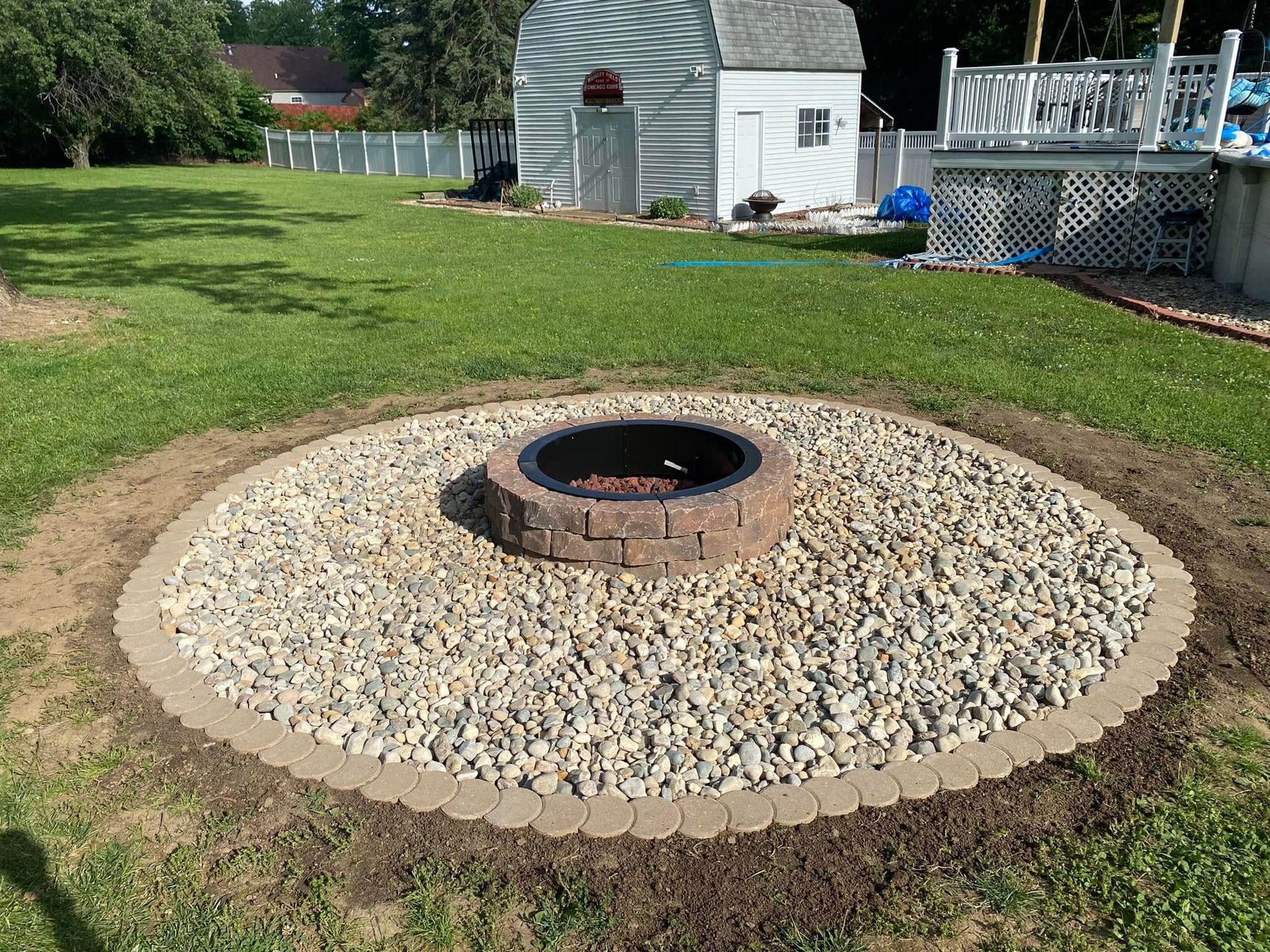 Backyard fire pit surrounded by gravel and a brick border on a grassy lawn