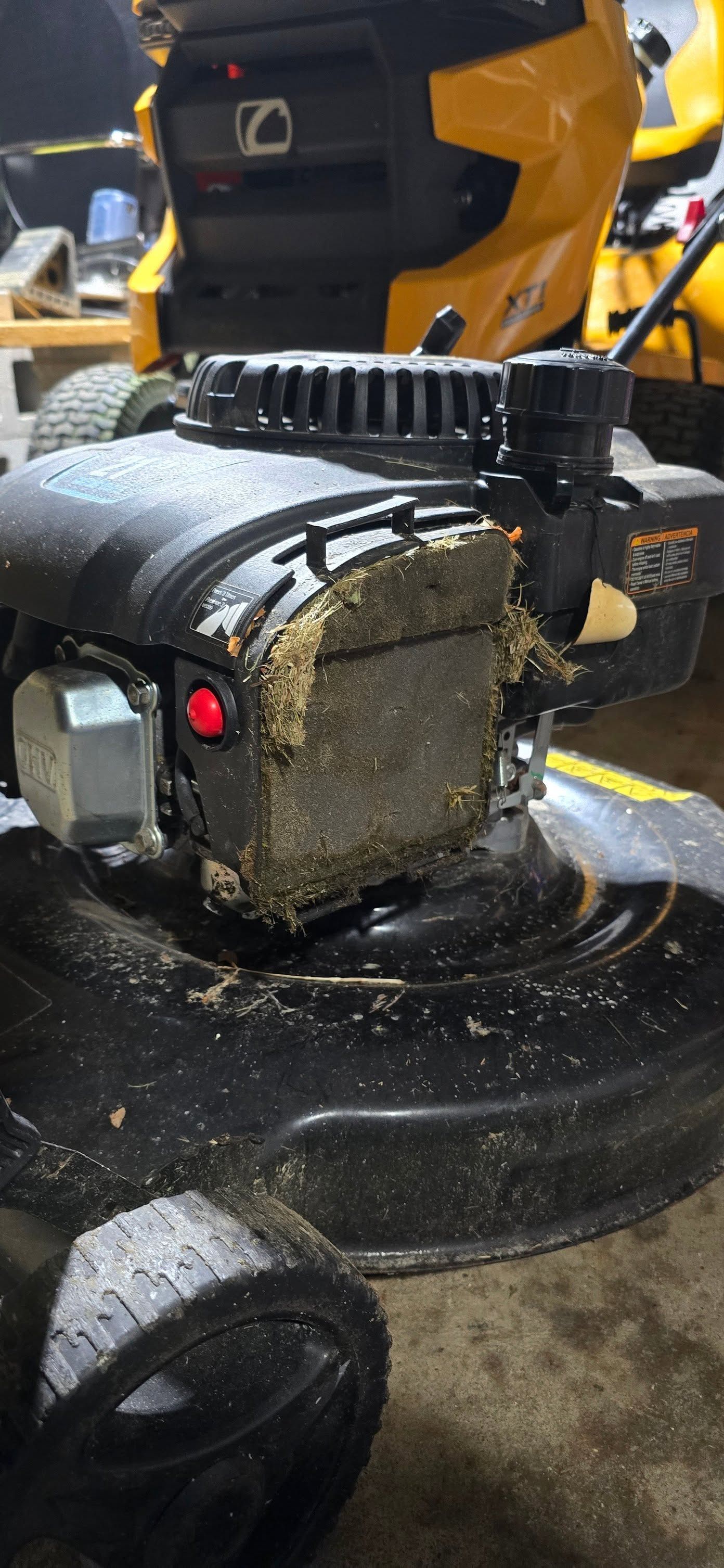 Close-up of a wet mower engine with a yellow body, black handle, and debris on the base.