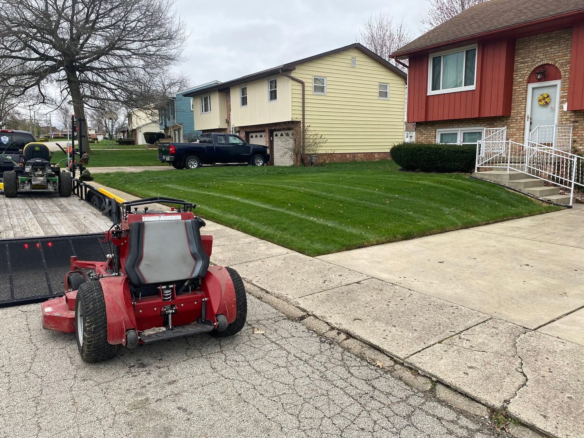 Red riding lawn mower on a driveway beside suburban houses and a grassy lawn