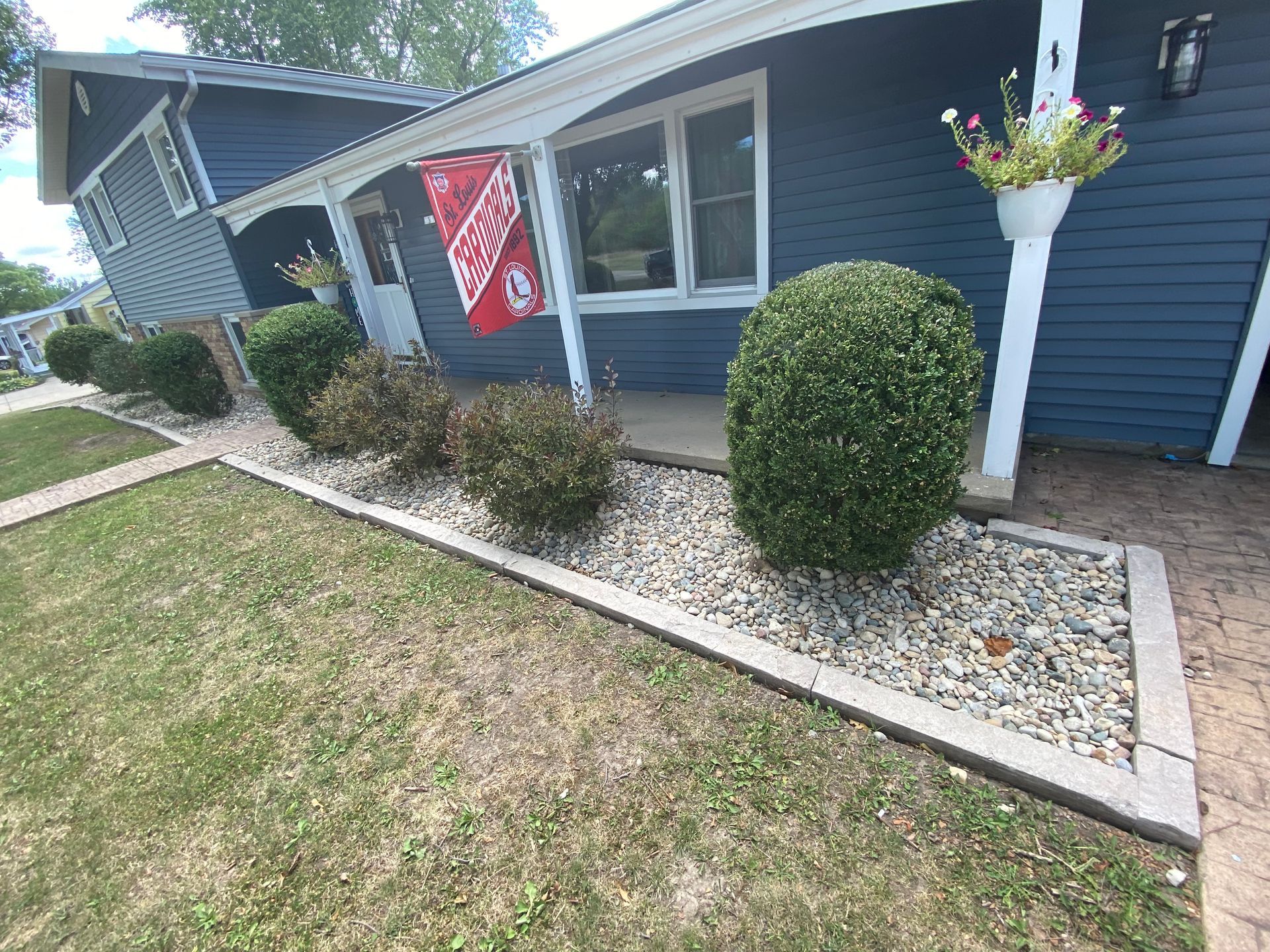 Blue house exterior with white trim, front walkway, shrubs, and a hanging flower basket