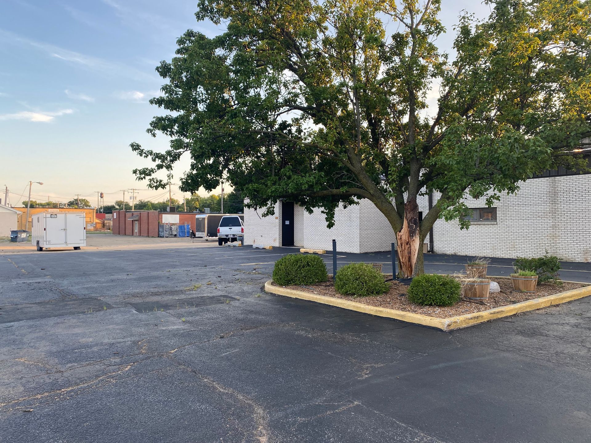 Empty parking lot beside a white building and trees at sunset