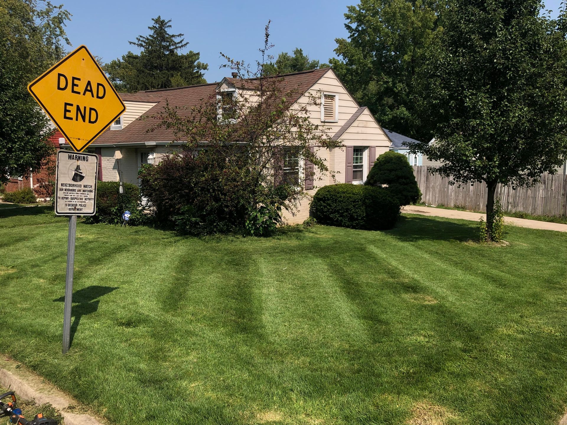Dead end street sign in front of a beige house with a green lawn and trees